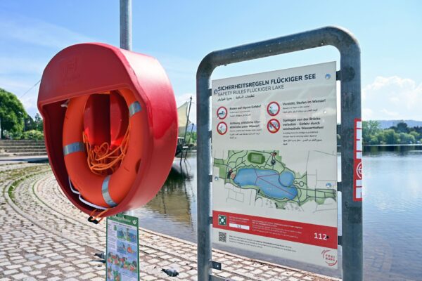 Neue Schilder am Flückiger See weisen in mehreren Sprachen auf Gefahren hin – hier wird auch der Einsatz von Rettungsringen getestet. Erst am gestrigen Dienstag gab es dort einen Sucheinsatz wegen eines mutmaßlichen Badeunfalls. Die groß angelegte Suchaktion verlief jedoch ergebnislos.